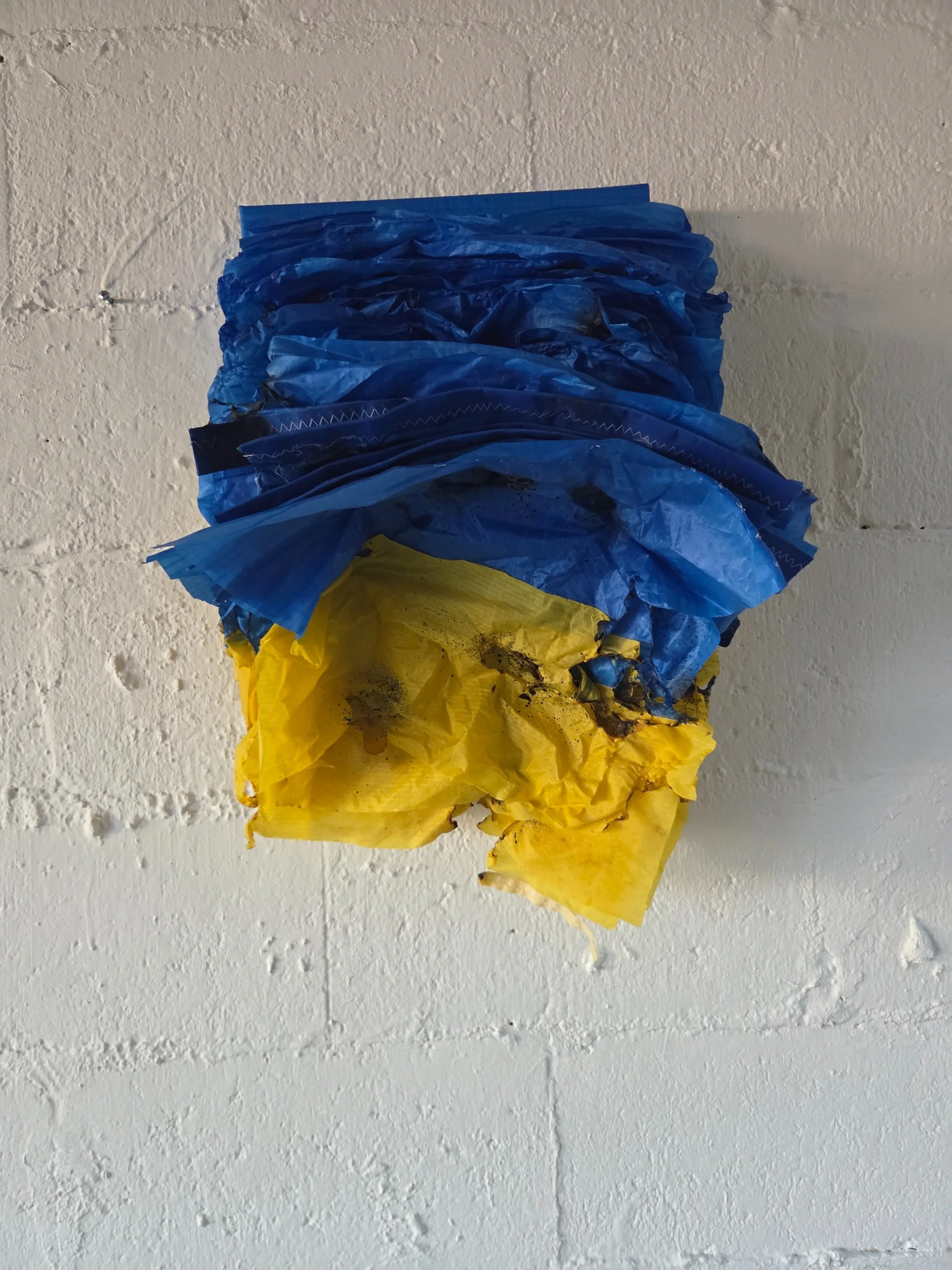 Layers of Freedom — stacked blue and yellow reclaimed sailcloth mounted on a white brick wall